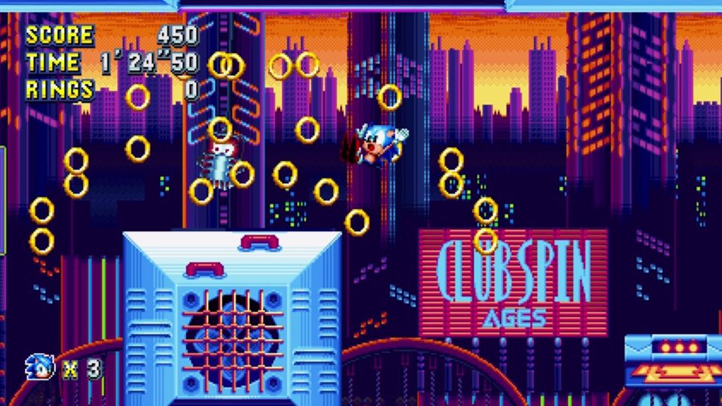 A screenshot of Sonic Mania for Mobile. Sonic looks to be in freefall against a city backdrop, with a dozen gold rings in the air around him.