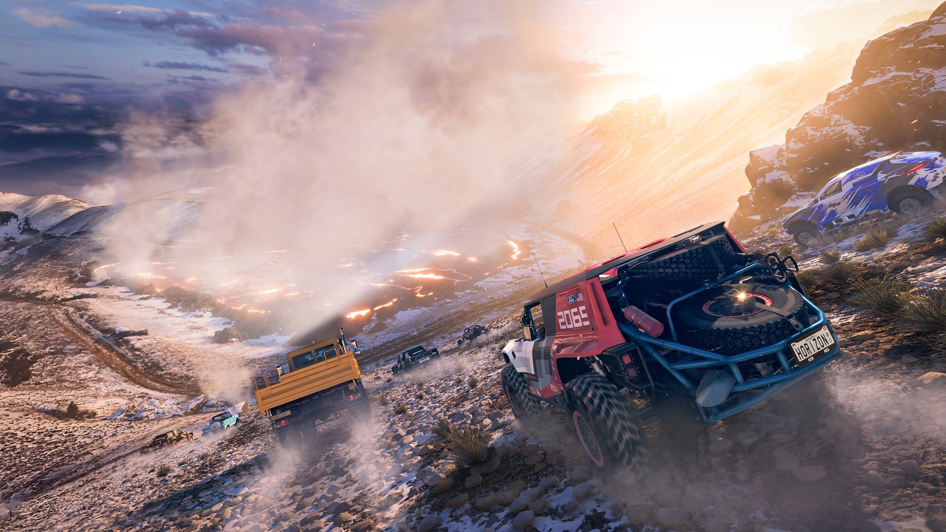 Off-road vehicles race up a snowy, mountainous trail at sunset, kicking up clouds of snow and dirt as they speed past rocks and rugged terrain.