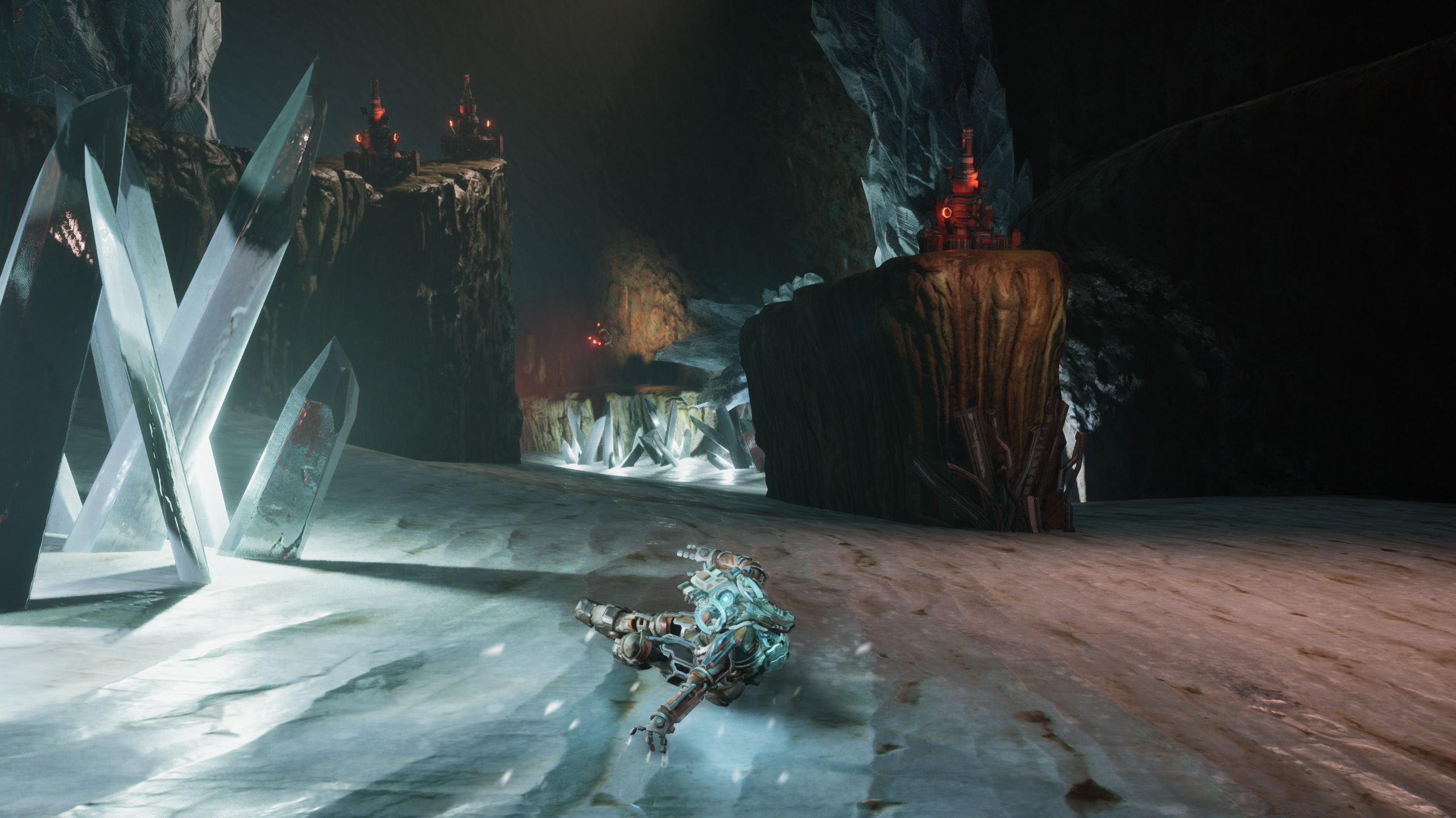 A concepting figure in futuristic armour slides on an icy cave floor surrounded by large crystals, with red-lit structures on rocky platforms in the background. The environment appears dark and otherworldly.